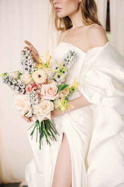 Close-up photo of a bride posing in an elegant dress holding a colorful bouquet