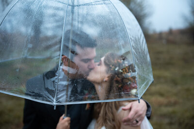 A newlywed couple kissing under a clear umbrella 