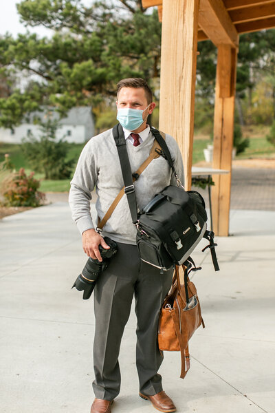 Brandon is outside a venue carrying a lot of photography gear and wearing a face mask.