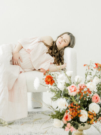 Pregnant woman in white dress holding belly surrounded by flowers