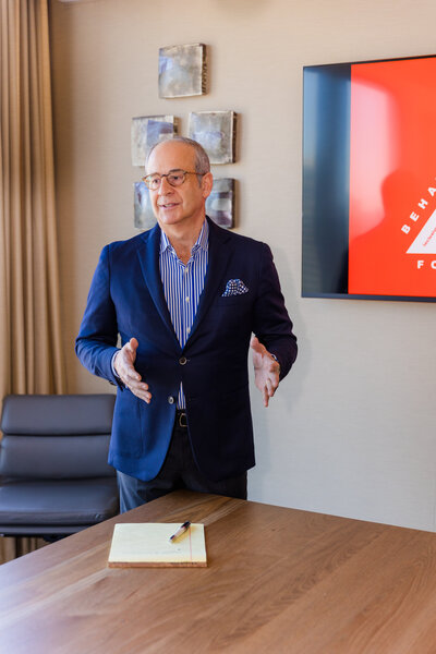Ahmet Bozer presenting in a conference room wearing a button-up shirt and jacket, looking at attendees off camera during his Atlanta Buckhead session