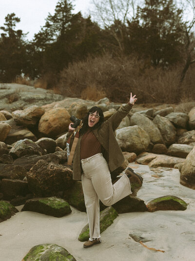 Photographer giving the peace sign and on the beach with their camera