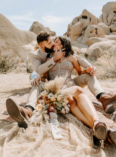 bride and groom sit in front of rock formations kissing