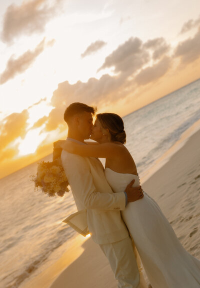 Bride and groom share a romantic kiss on the beach at sunset during their Cancun destination wedding.