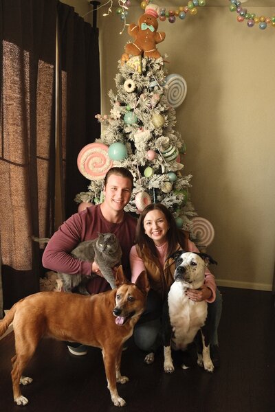 Logan Ferree and her husband posing with their two dogs in front of a Christmas tree at home.