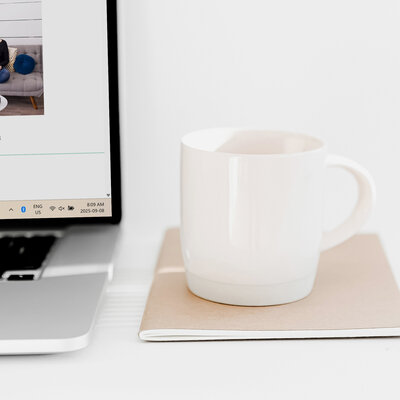 Open laptop with a coffee mug and notebook on a white desk, representing HoneyBook tips and systems for wedding photographers.