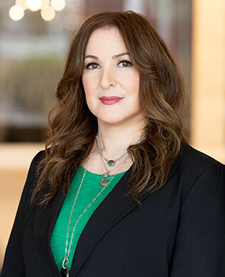 Headshot of a woman with long brown hair wearing a blue blazer and blue and white polka dot blouse