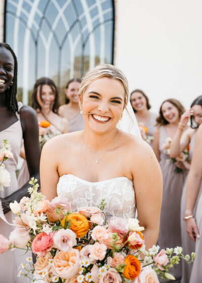 A joyful bride smiles as she holds her colorful wedding bouquet.