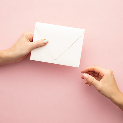 hand holding white envelope on pink background