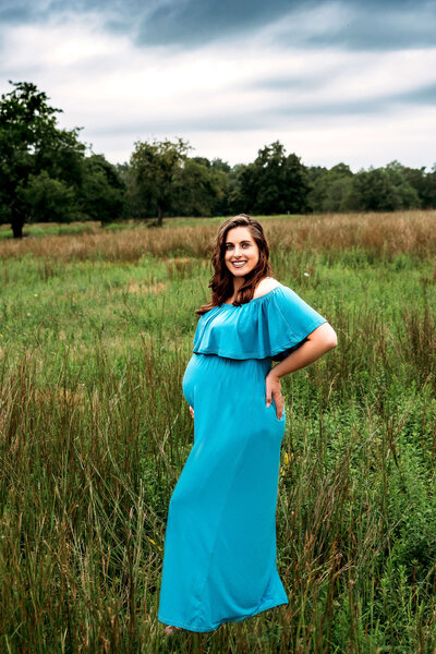 Radiant pregnant woman in bright blue ruffled dress poses in golden grassland during natural light Connecticut field maternity session