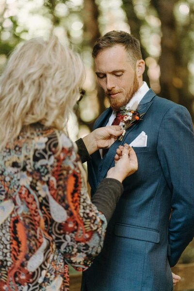 DelJean, a florist in Eugene, Oregon, pins a boutonniere on a groom at a wedding.