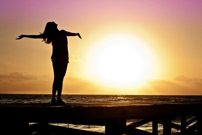 Silhouette of a woman with outstretched arms at sunset, symbolizing freedom and personal growth through life coaching