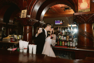 shot of bride and groom at bar taking a drink and kissing