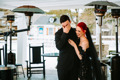 A photo of a groom crying while a bride with red hair and a black dress hugs him at a non-traditional wedding in Connecticut