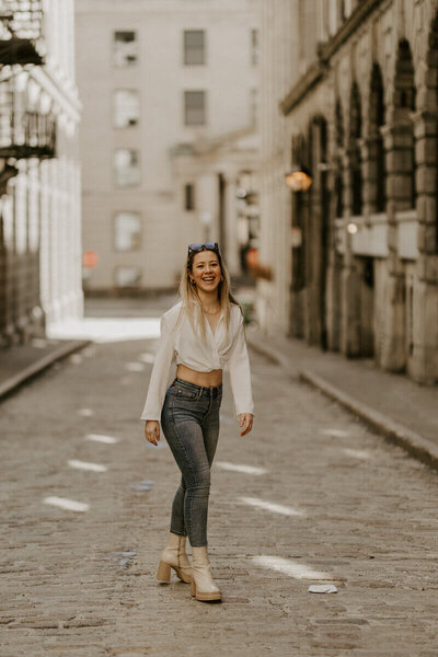 Femme en jean et chemise blanche, marchant dans une rue pavée vide de Montréal capturée par Laura, photographe portrait.