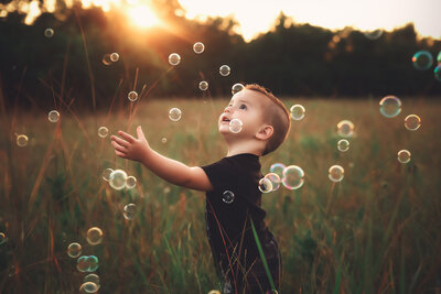 little boy playing with bubbles in the field