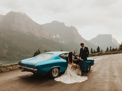 Bride and groom posing in front of their blue classic car in Glacier National Park.
