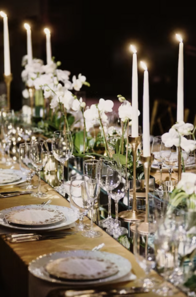 Luxurious dinner setup featuring tall candles and elegant floral arrangements on a beautifully set table, creating a warm and sophisticated atmosphere.