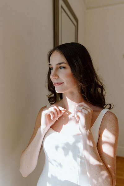 Bride fixing necklace by a window
