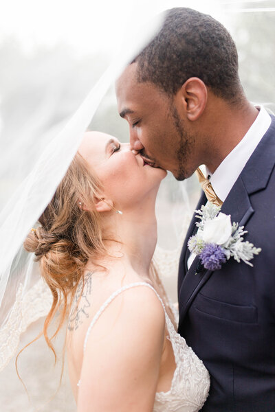 bride and groom kissing under veil photographed by Kaitlin Mendoza Photography, a wedding photographer in Indianapolis