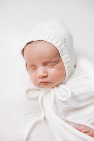 studio portrait of newborn baby girl in white bonnet on white backdrop by fine art photographer Samantha Jay