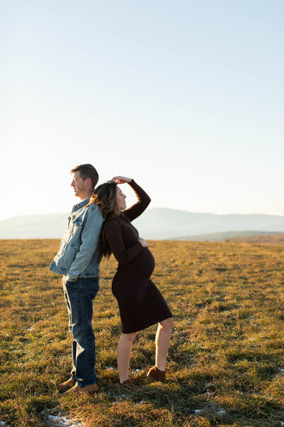 Pregnant couple lean back to back against each other in a field