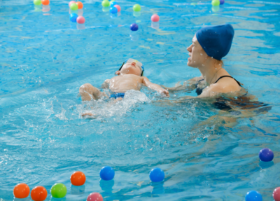 A swim coach gently teaches a baby to float, creating a positive introduction to water