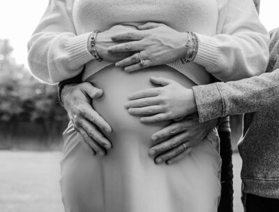 Mom, dad, and older sibling with their hands on the stomach of pregnant mom.