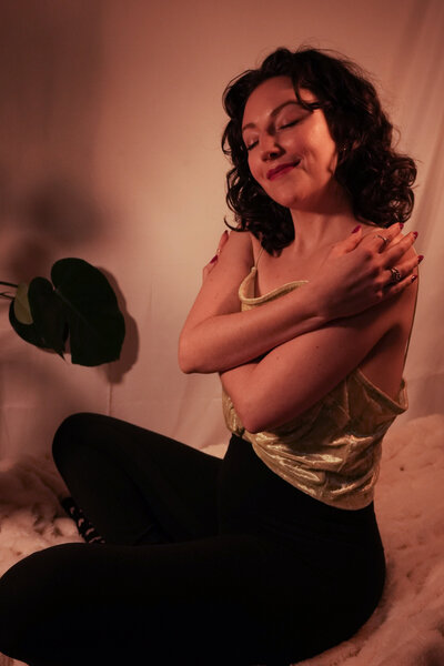 An intuitive healer sitting on the floor with her hands in her hair, wearing a green shirt and smiling. The healer's relaxed and confident expression suggests a sense of peace and well-being. This image is perfect for anyone seeking a calm and healing energy. [Nicole QW]