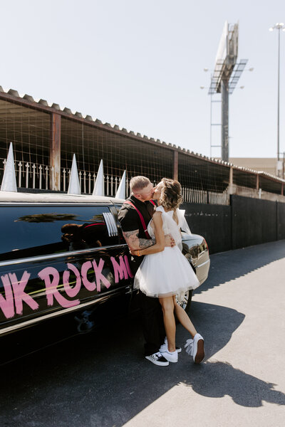 A newlywed couple kissing while leaning up against a black limo 