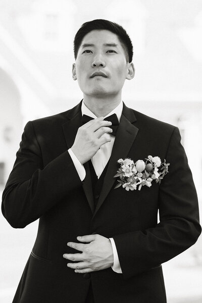 Black and white portrait of groom adjusting his bowtie