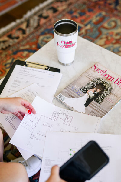 Wedding floor plans, clipboard, and magazine laid out on a table with a tumbler labeled “Chaos Coordinator” — behind-the-scenes of Austin wedding planning.