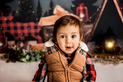 Portrait Photographers CT capture charming baby boy in buffalo plaid outfit with sherpa vest at rustic camping themed first birthday session