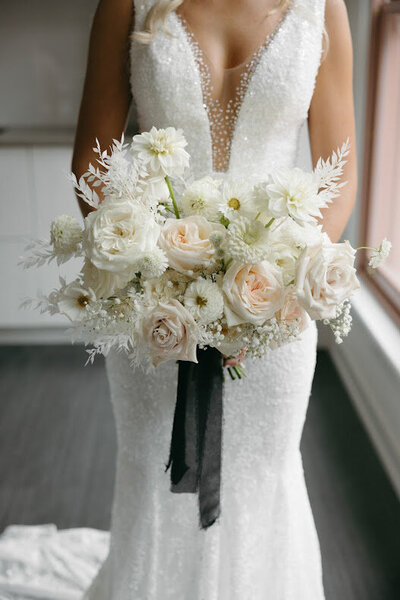 Close-up of a bride holding her all-white floral bouquet with black ribbon, showcasing modern elegance. Perfect for couples seeking wedding florals in Ottawa.