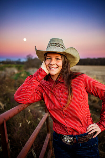 Senior Girl wearing cowboy hat and red blouse on county Ohio farm smiling with moon in background