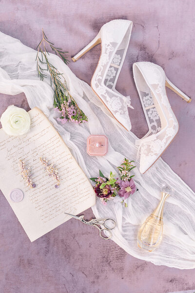 a brides bella belles wedding shoes, perfume, and jewelry laying on a velvet purple background.