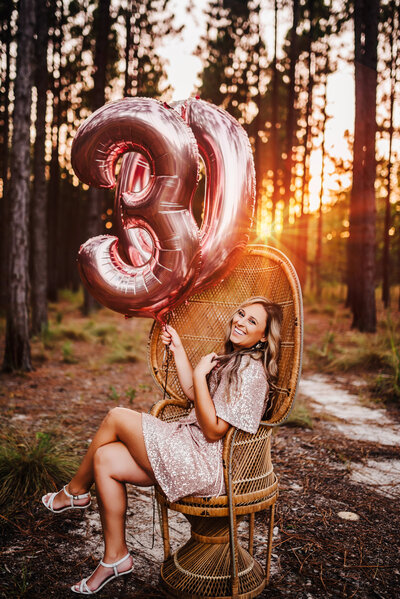 a 30th birthday photo of a woman holding  a 3 and a 0 balloons during sunset