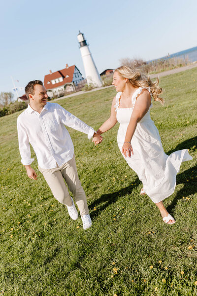 Man and woman walking at Portland Headlight while holding hands and smiling at each other