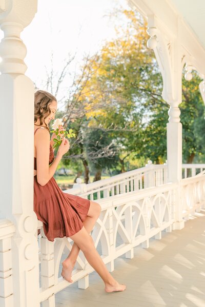 High school senior wearing an orange dress and sitting on a white porch railing by Oak Park, IL senior photographer Kristen Hazelton