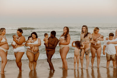 Women of all sizes and skin tones stand on the beach with their babies