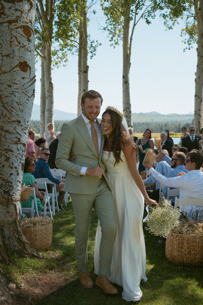 Newlyweds walking hand-in-hand back down the aisle, smiling and celebrating with guests after their ceremony.