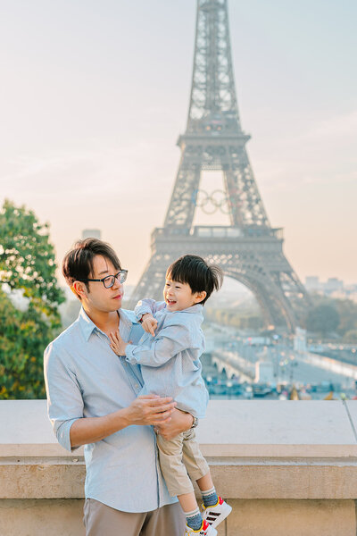 Mother holding her young son as they smile at the camera with the Eiffel Tower in the background at Trocadéro during a Paris family photoshoot.