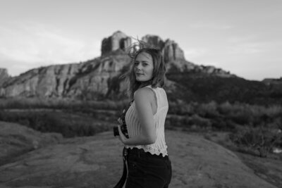 Brisa holds film camera in black and white with Sedona rocks behind.