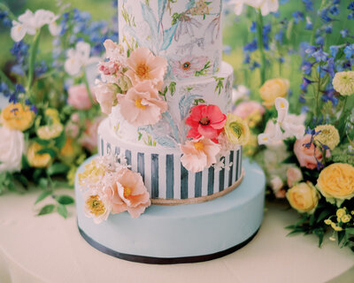 A blue cake with vibrant flowers sits on a table.