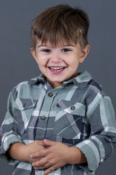 Preschool boy wearing a blue plaid shirt laughing for his school photo