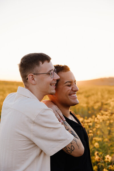 Two people standing close together smiling at sunset