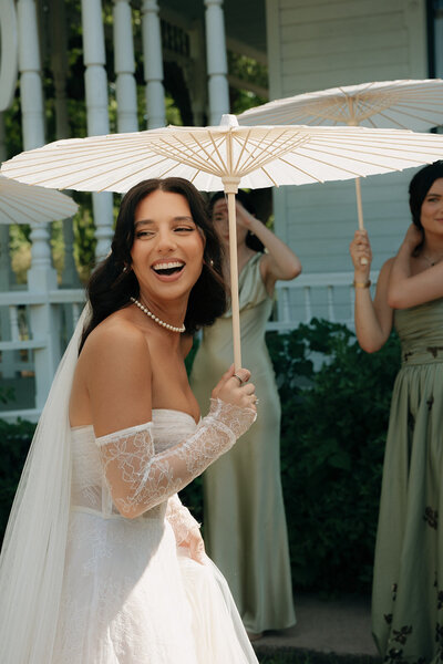 Bride and her bridesmaids in green dresses holding white umbrellas