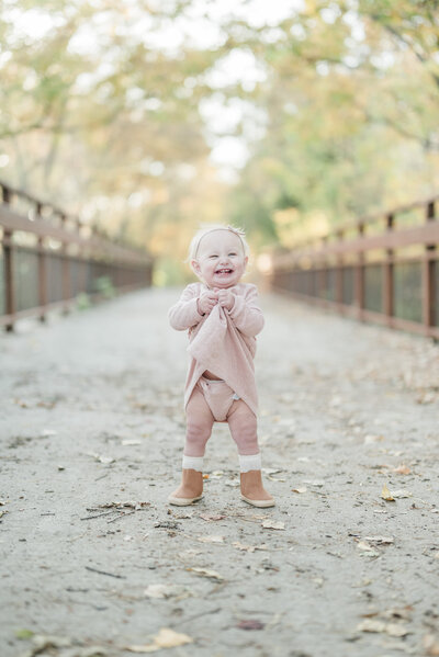 Smiling toddler standing in the center of a rustic wooden bridge during a Kansas City petite photography session.
