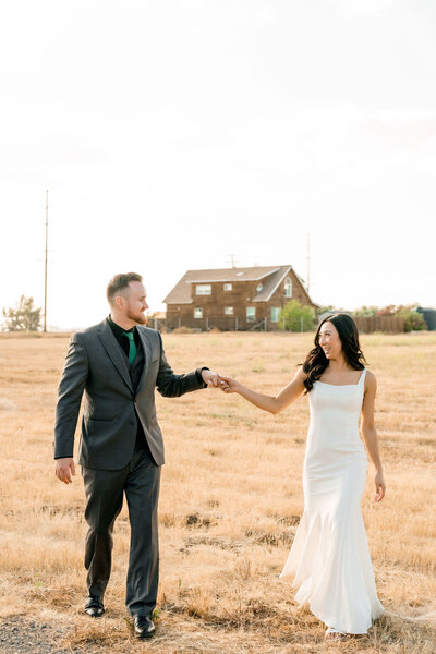 bride and groom reaching out and holding hands while walking in a field