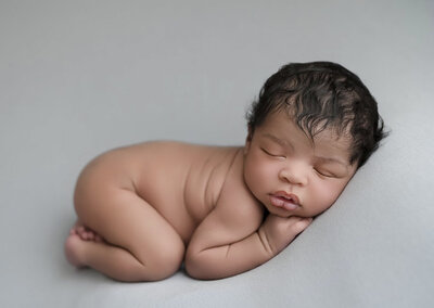 baby girl lying on stomach bare skin and against a teal blanket covering a beanbag.